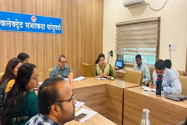 लकड़ी की मेज के चारों ओर बैठकर दस्तावेज देखते और नोट्स लिखते अधिकारी